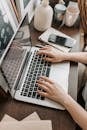 From above of unrecognizable woman sitting at table and typing on keyboard of computer during remote work in modern workspace